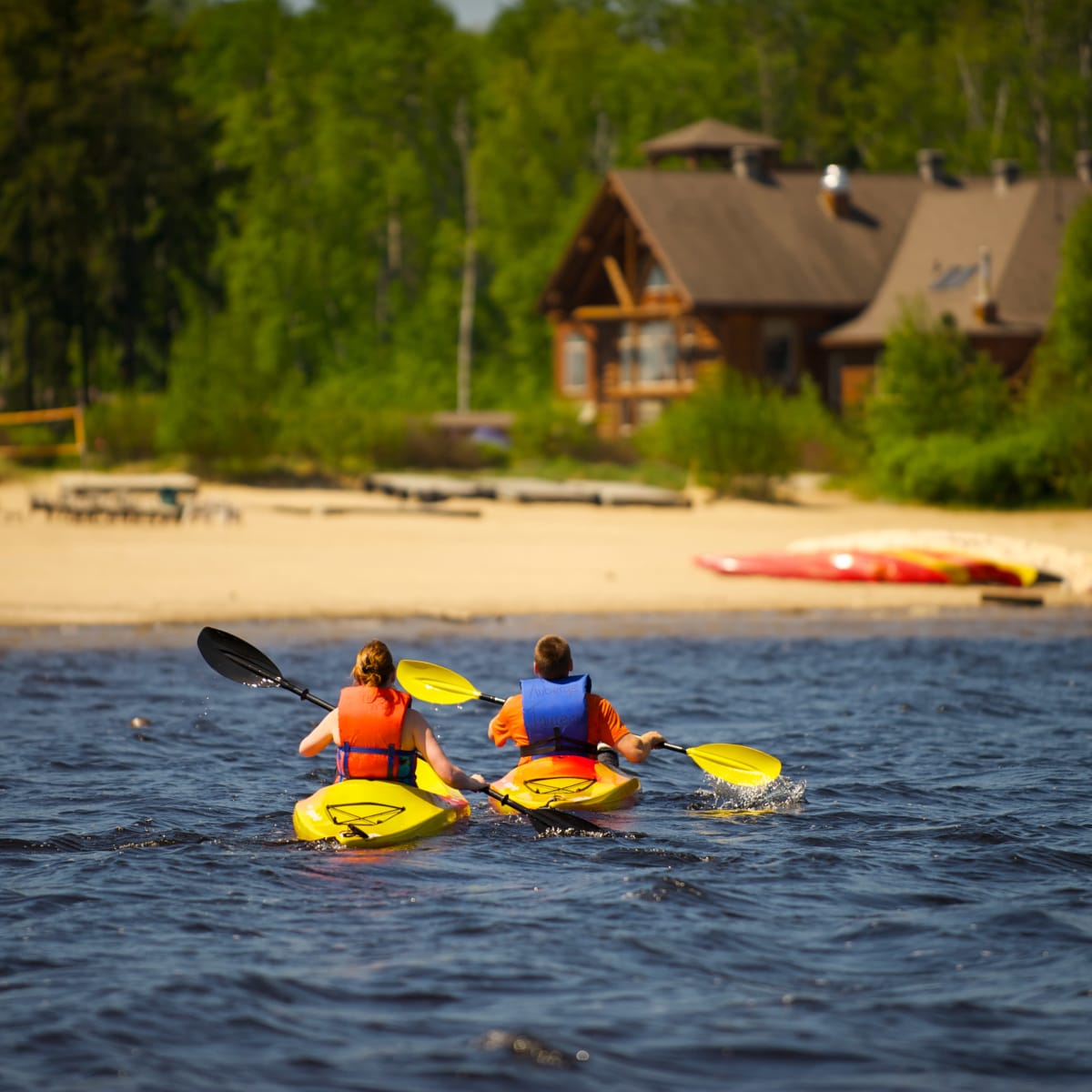 Deux personnes en kayak sur un plan d'eau bordé d'une plage de sable.