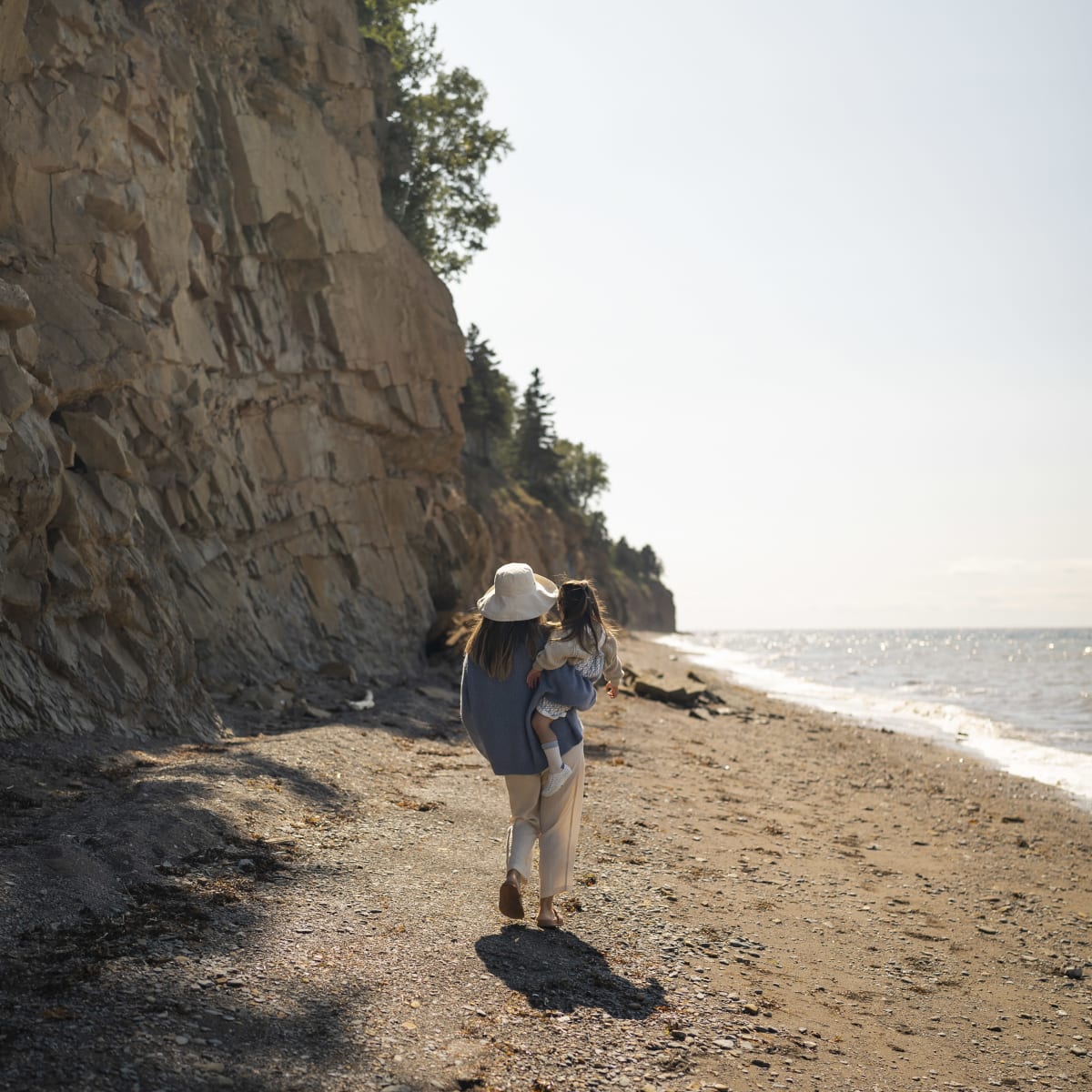 Une mère et son enfant sur une plage bordée d'un cap rocheux.