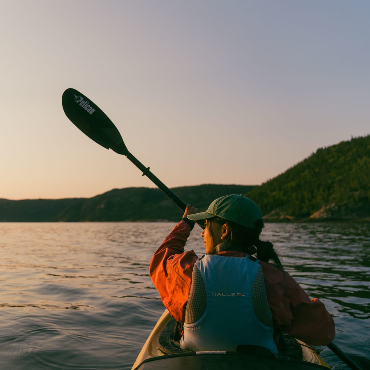 Femme en kayak sur le fjord au coucher de soleil.