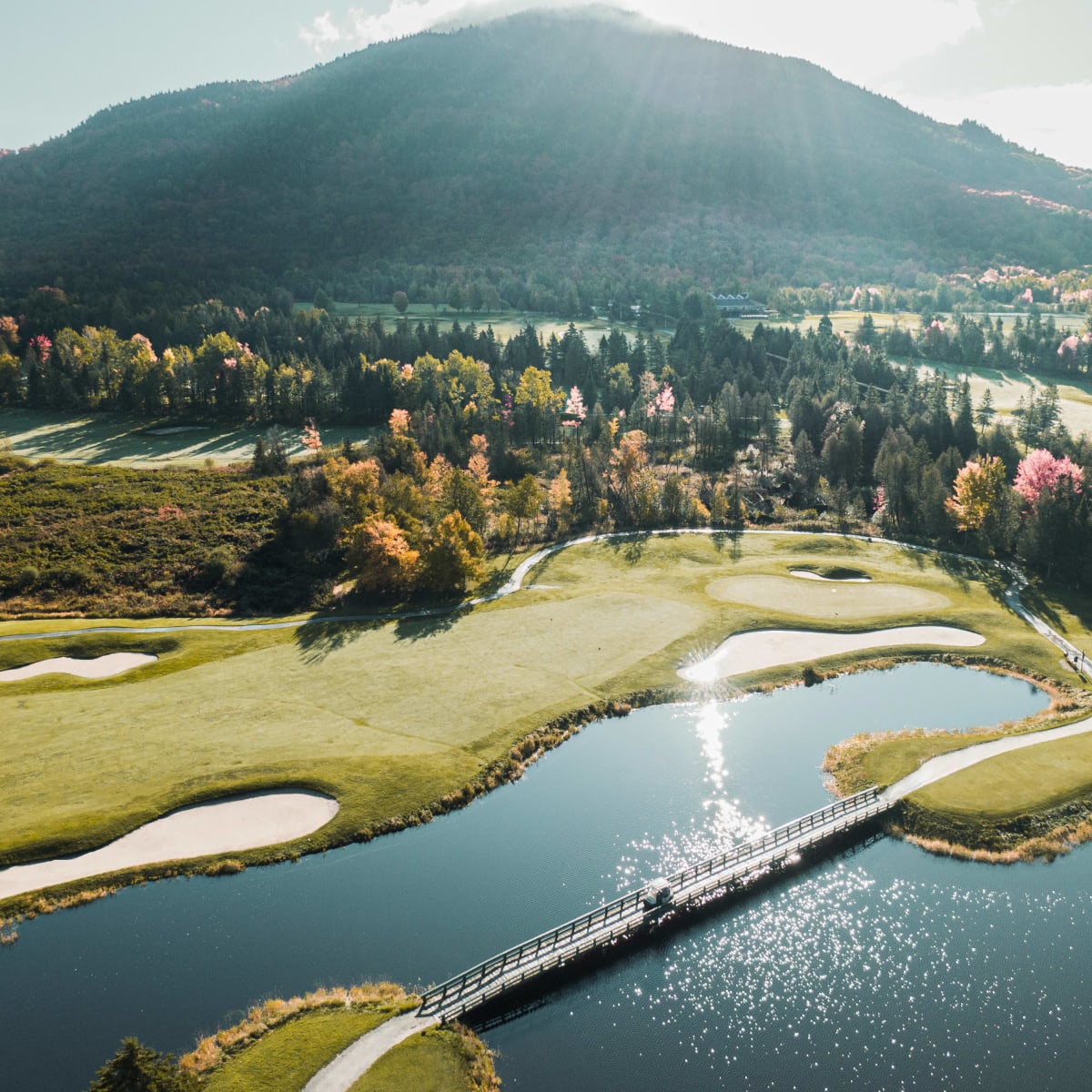Vue aérienne des verts et plans d’eau du golf Owl's Head en automne, avec une montagne en arrière-plan.