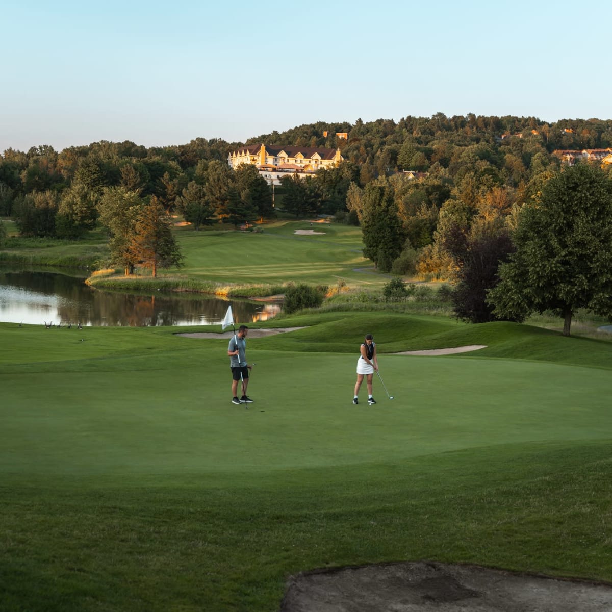 Deux golfeurs se tenant sur un vert, avec le Château Bromont en arrière-plan.
