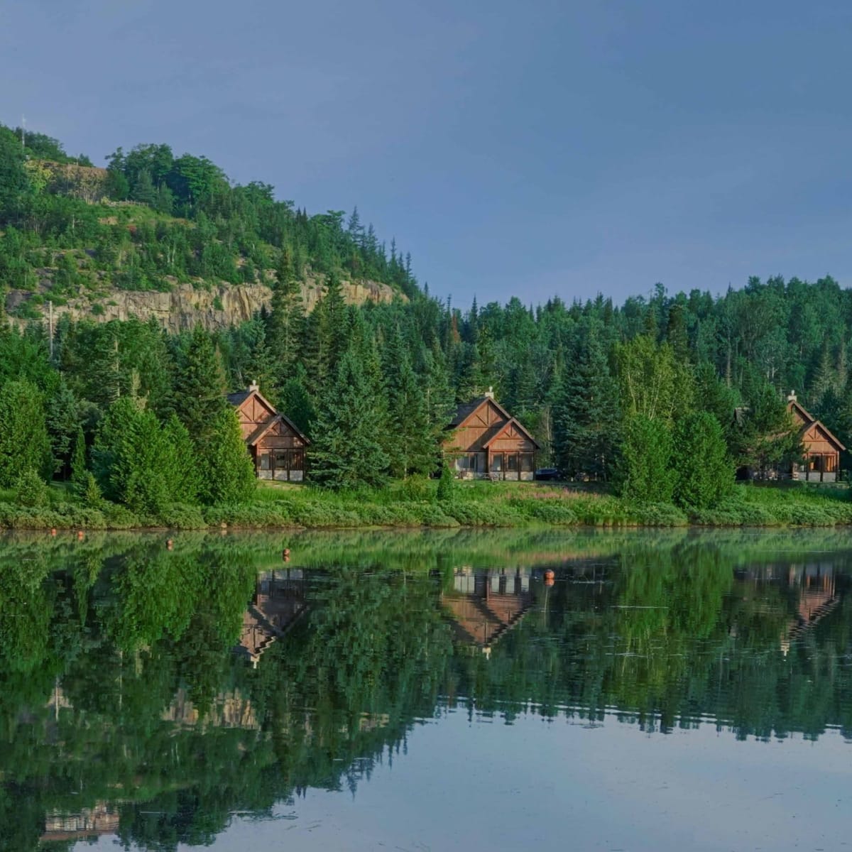 Alignements de cinq Chalets Royal Laurentien au bord d'un lac dans un paysage verdoyant.