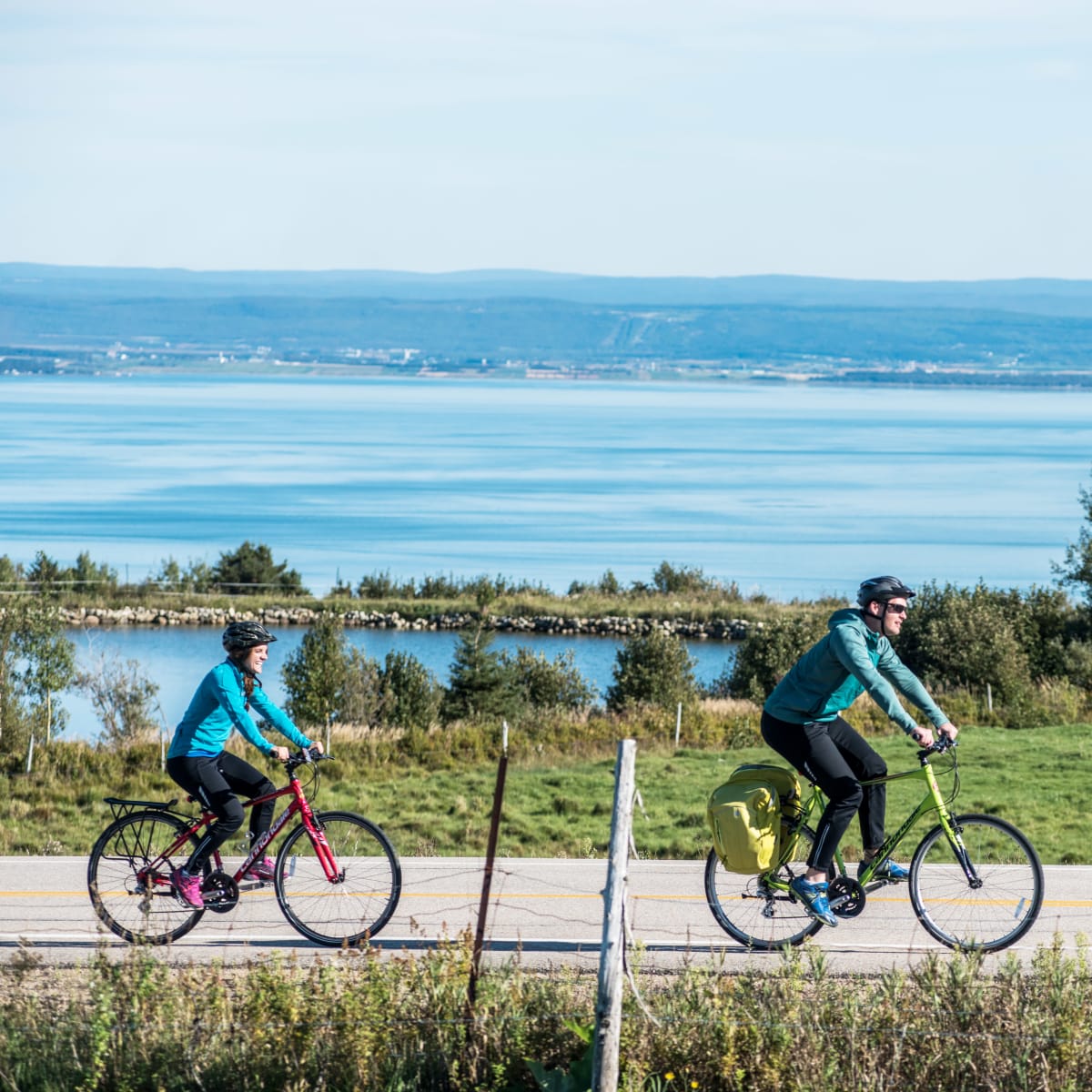 Deux cyclistes en train d'explorer la région de Charlevoix à vélo, avec le fleuve en arrière-plan.