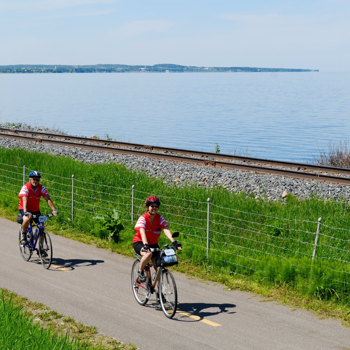 Deux cyclistes sur une piste asphaltée bordée d'un chemin de fer et d'un cours d'eau