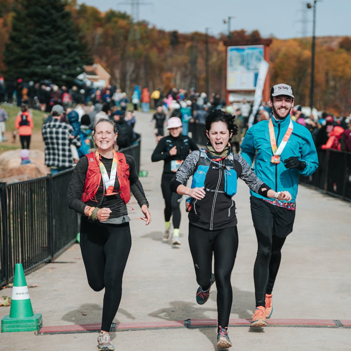 Défi des Couleurs Simard - Trois personnes franchissent la ligne d'arrivée d'une course, avec une foule en arrière-plan.