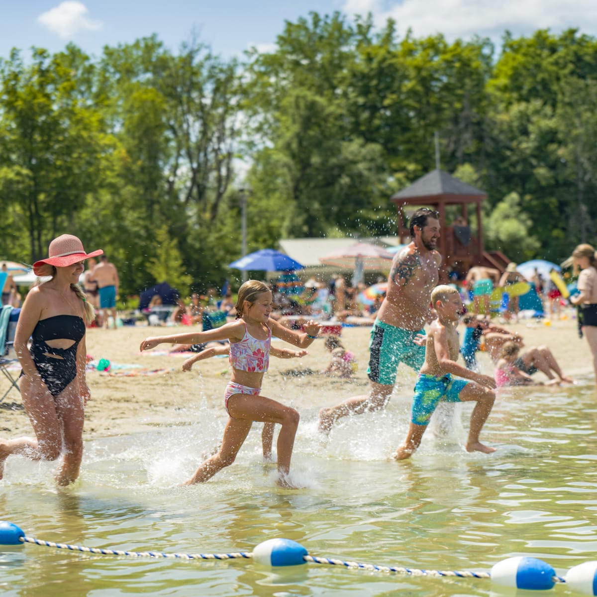 Famille courant vers l'eau à la plage du parc régional des Îles-de-Saint-Timothée