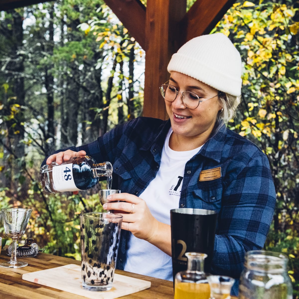 Distillerie du Fjord - Une femme prépare un breuvage alcoolisé, nature en arrière-plan.