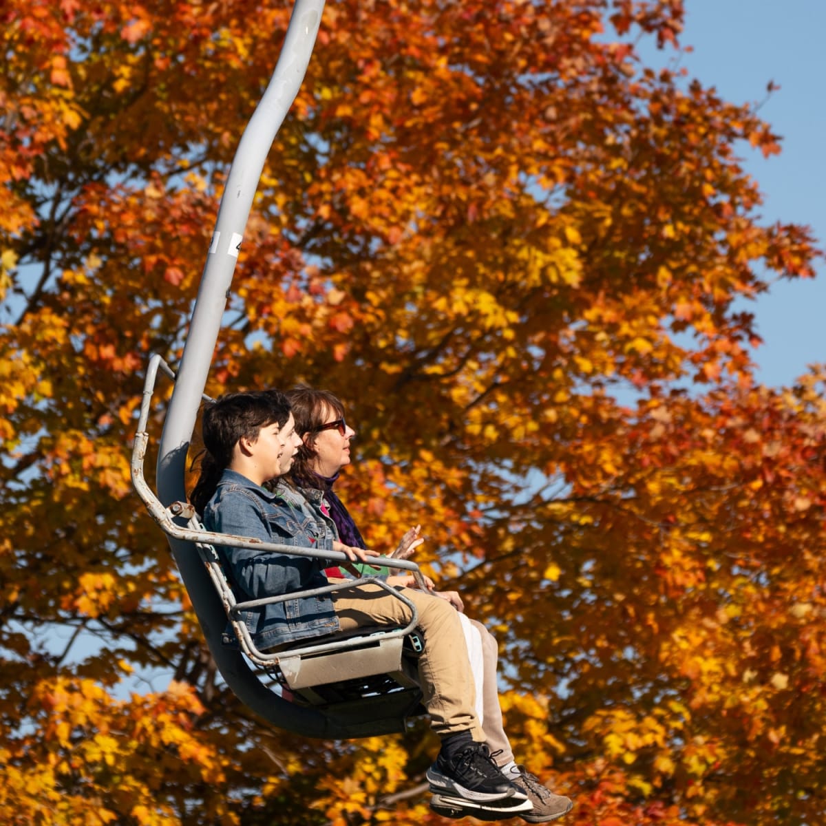 Two adults on a ski lift at Ski Saint-Bruno in the fall.Fall foliage galore!