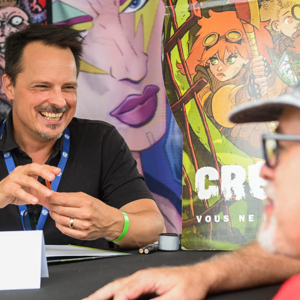 Prévost Comic Arts Festival - A cartoonist is seated with another man and is smiling.