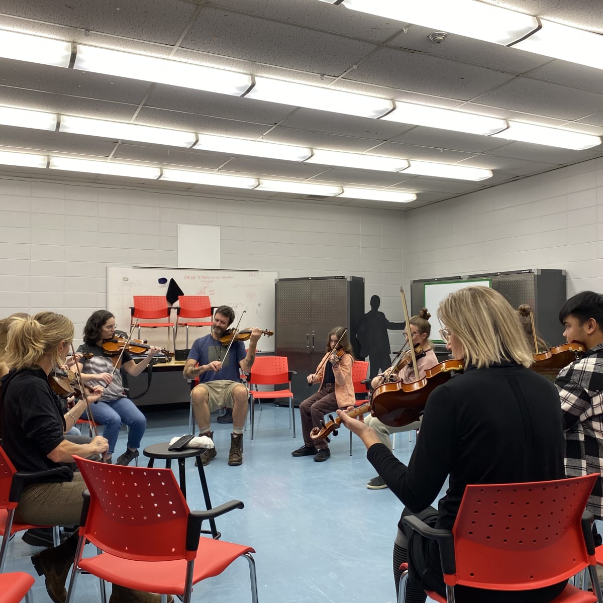 Val-d'Or Traditionnal Music Festival - Individuals are seated on red chairs in a circle, playing violins.