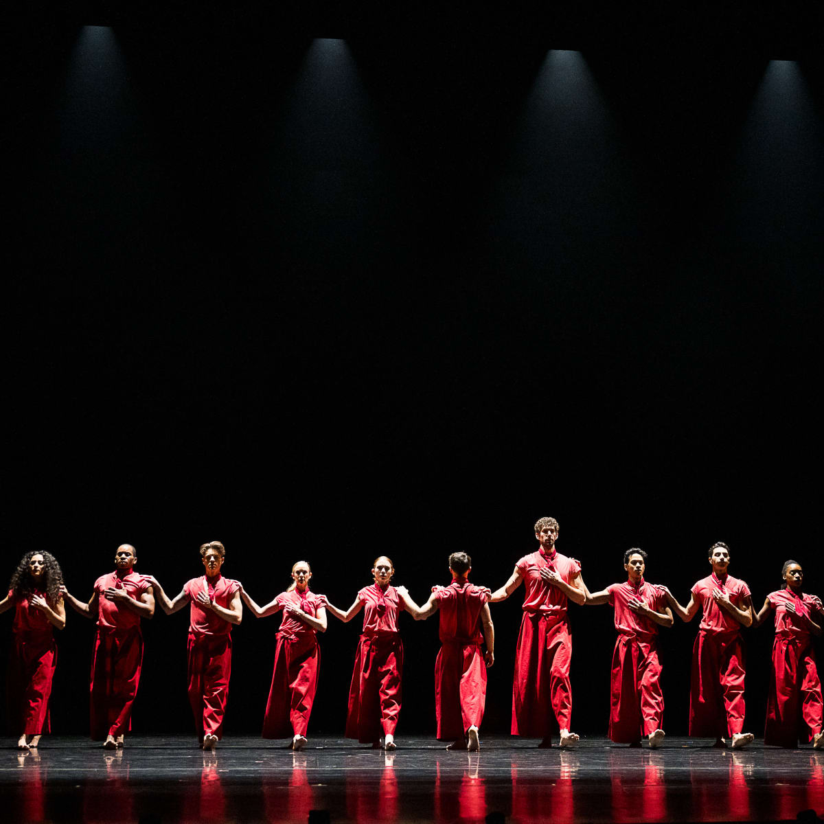 Festival des Arts de Saint-Sauveur - Des danseurs habillés en rouge sont disposés en ligne sur une scène noire