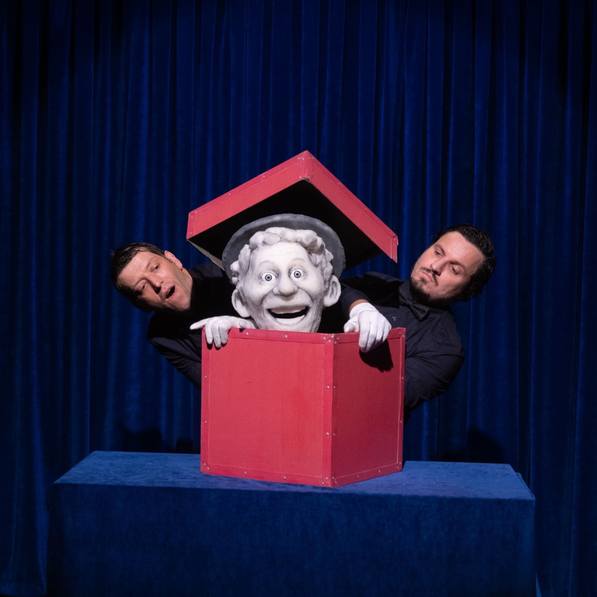 Festival international des arts de la marionnette - Une marionnette est dans une boîte rouge. Deux hommes sont à côté.