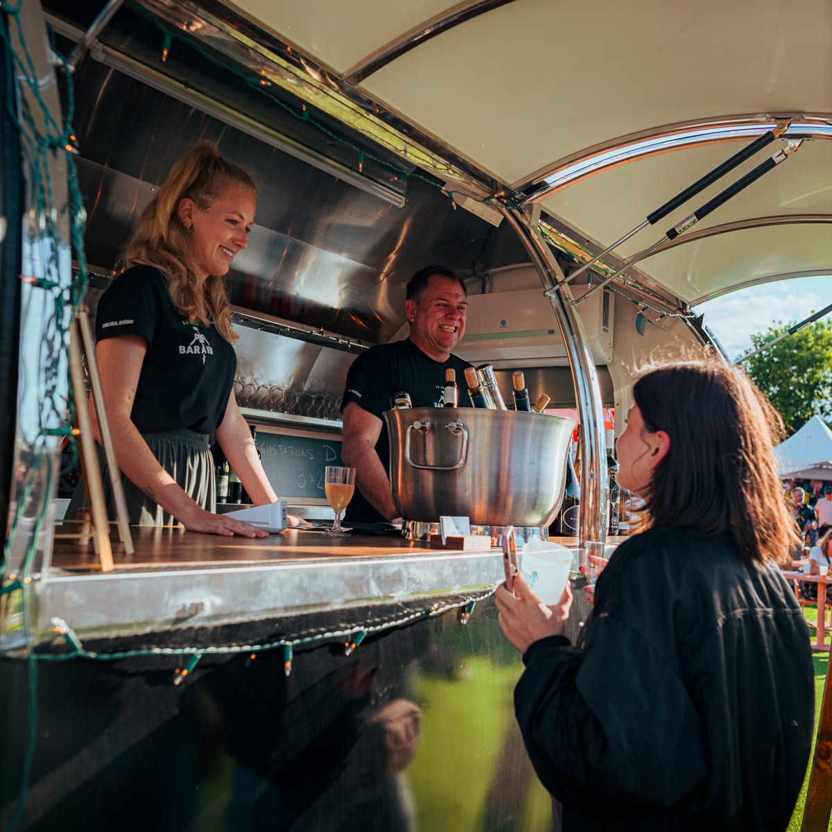 Festival Parasol - Une femme discute avec deux vendeurs souriants qui sont dans un bar mobile