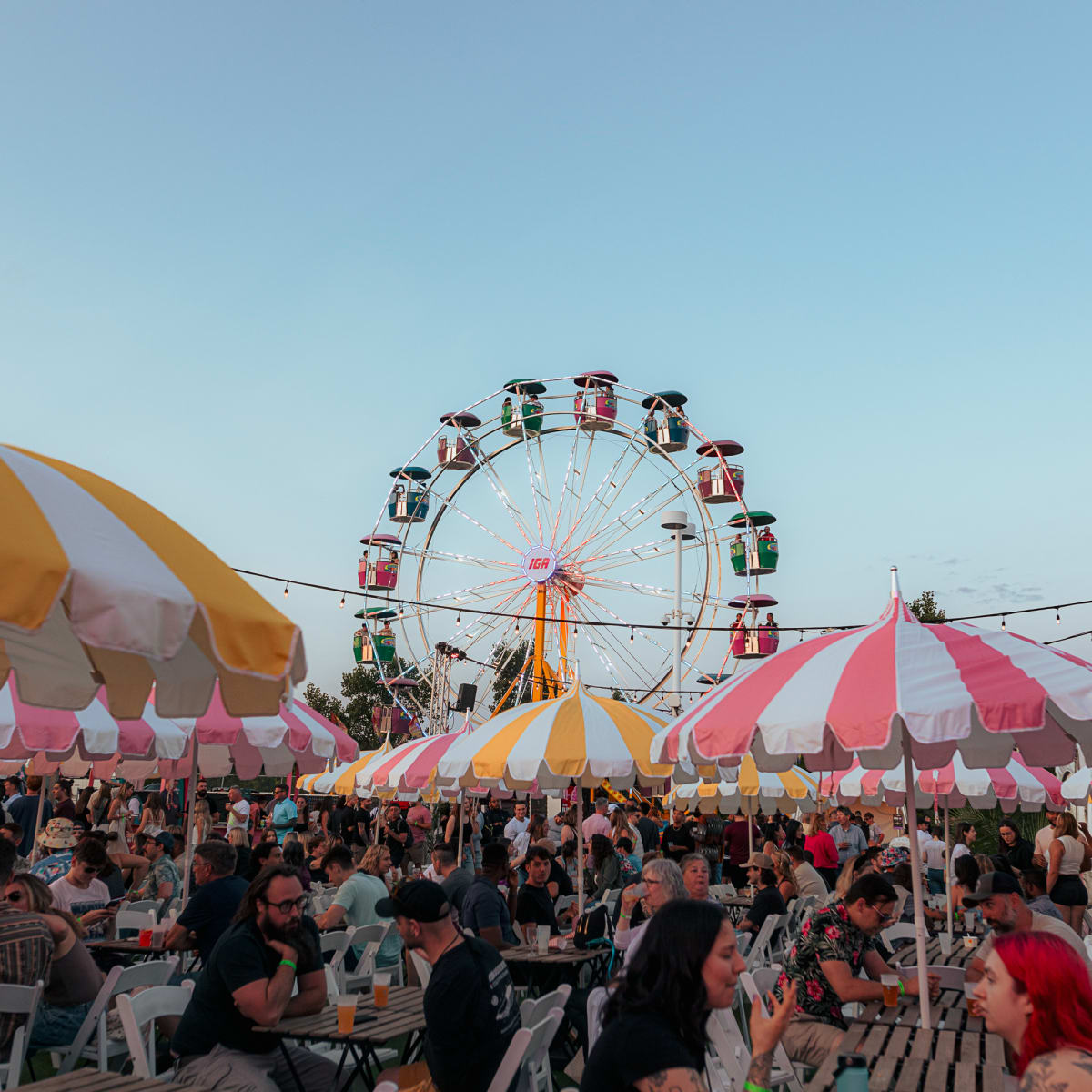 Festival Parasol - Des gens sont assis à des tables avec parasols, avec une grande roue en arrière-plan