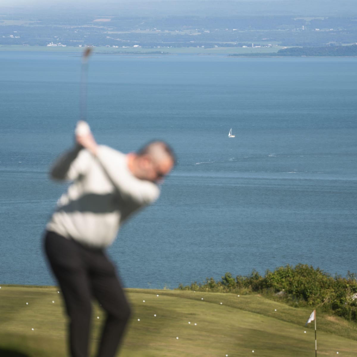 Golfeur en train de s'élancer au Golf Manoir Richelieu; le focus est sur le fleuve en arrière-plan plutôt que sur l'homme.