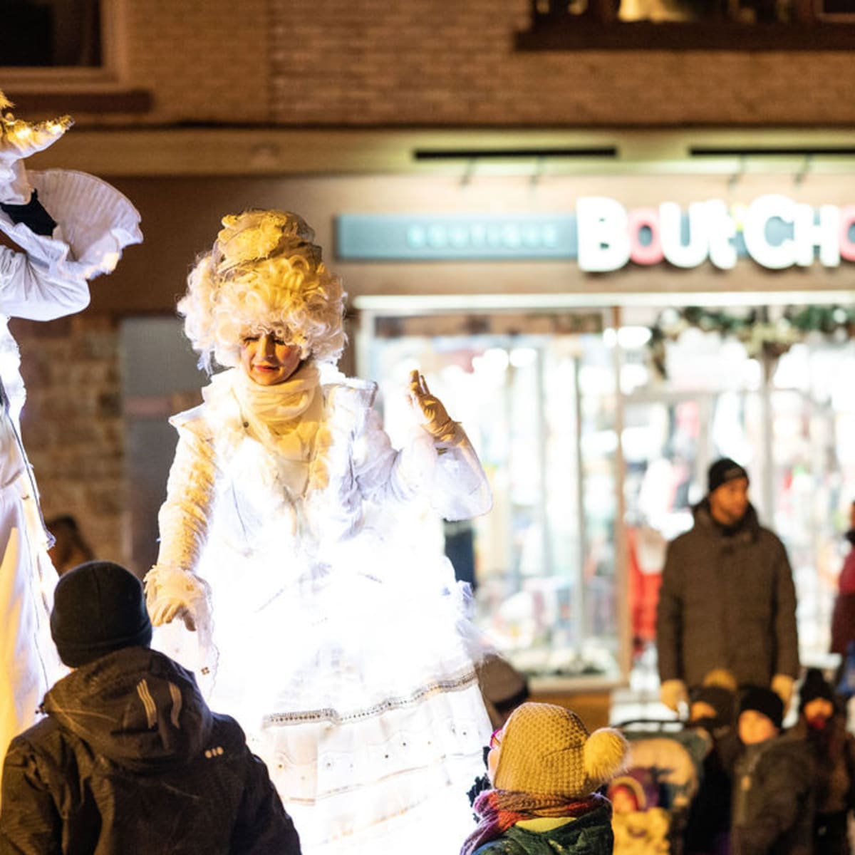 Artists dressed in glowing white costumes greeting children during a festive event.
