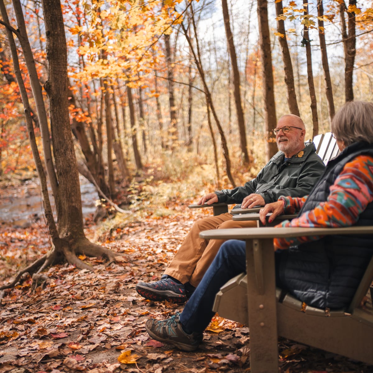 Municipalité d'Orford - Un couple assis sur des chaises de bois dans une forêt aux couleurs automnales