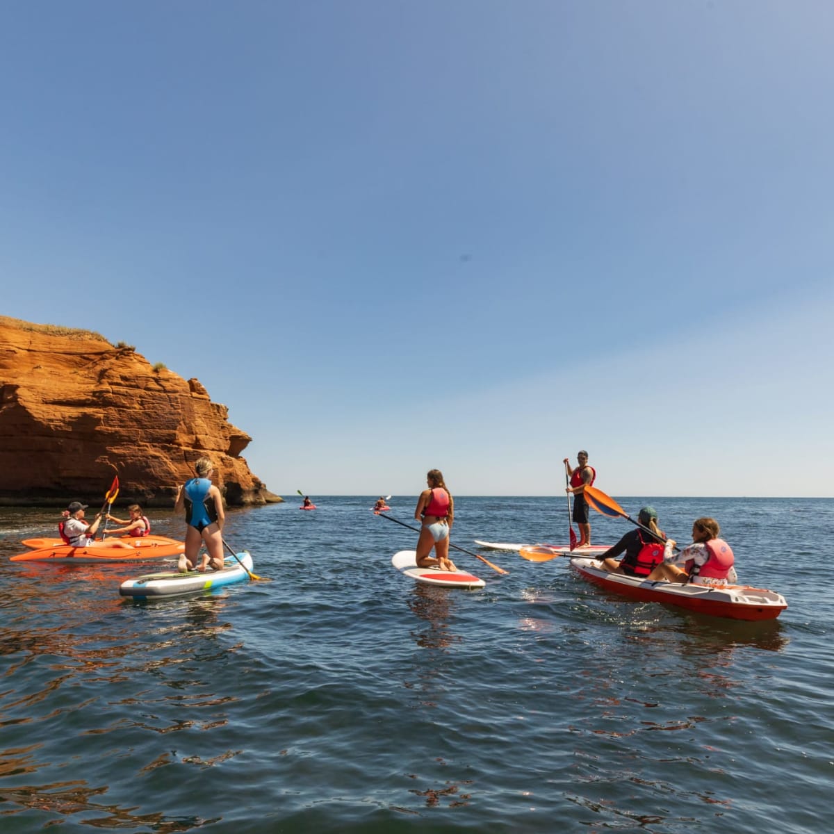Groupe de personne en planche à pagaie et autres embarcations nautiques à proximité des falaises rouges au Parc du Gros-Cap.