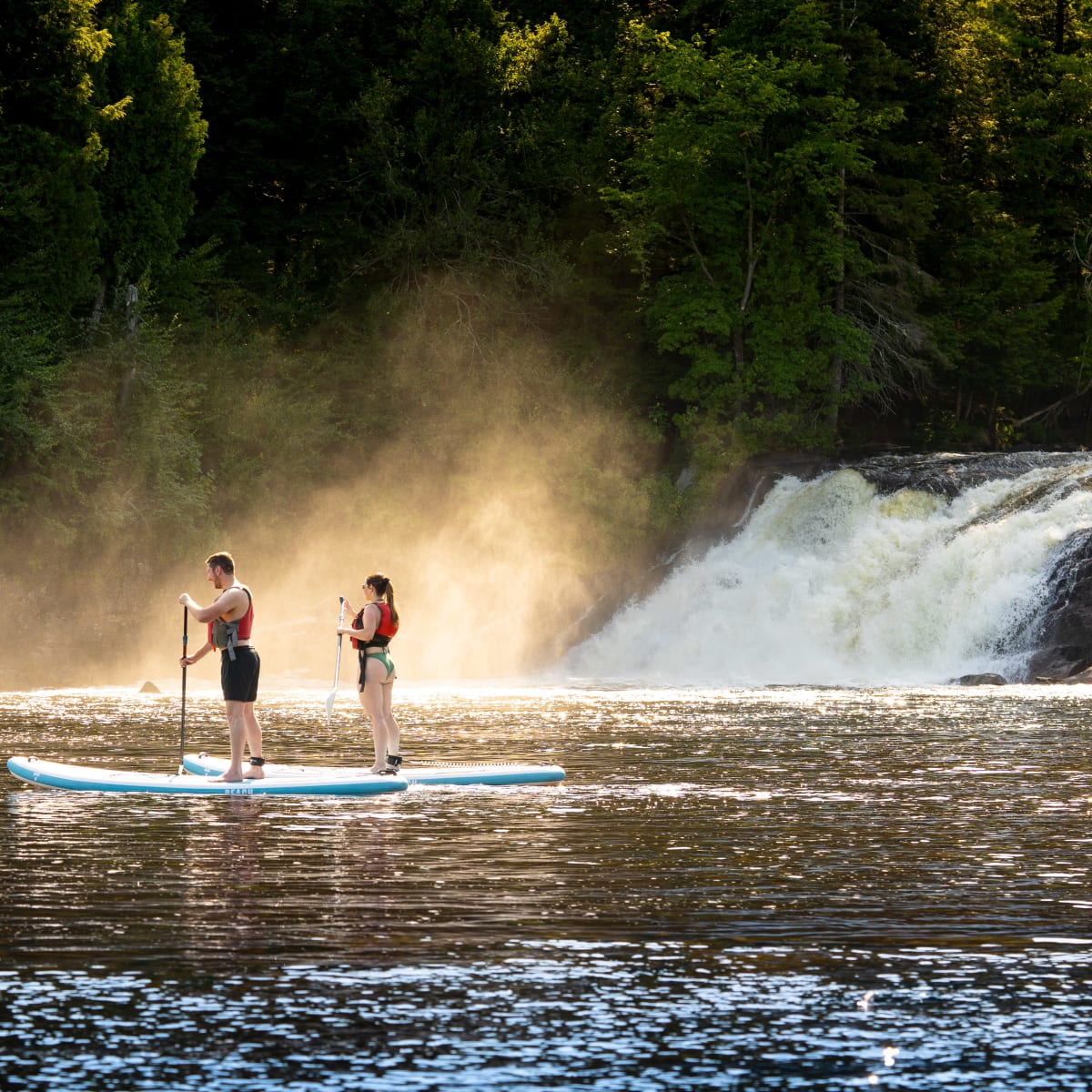 Deux personnes en planche à pagaie, avec une chute d'eau en arrière-plan.