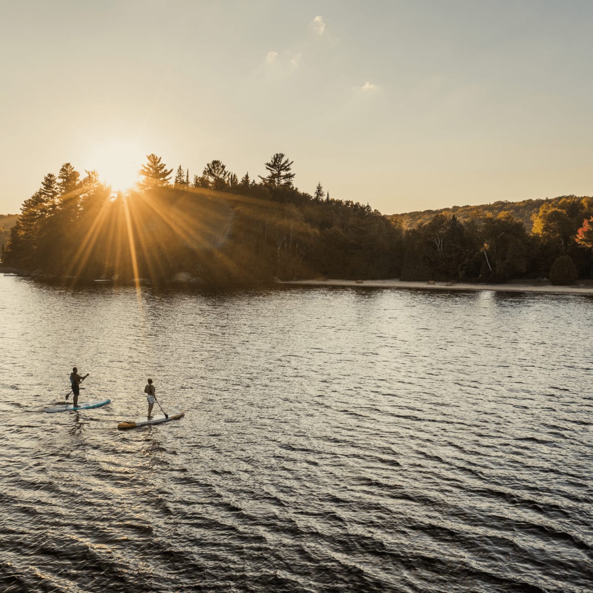 Deux personnes en planche à pagaie sur un lac au coucher du soleil.