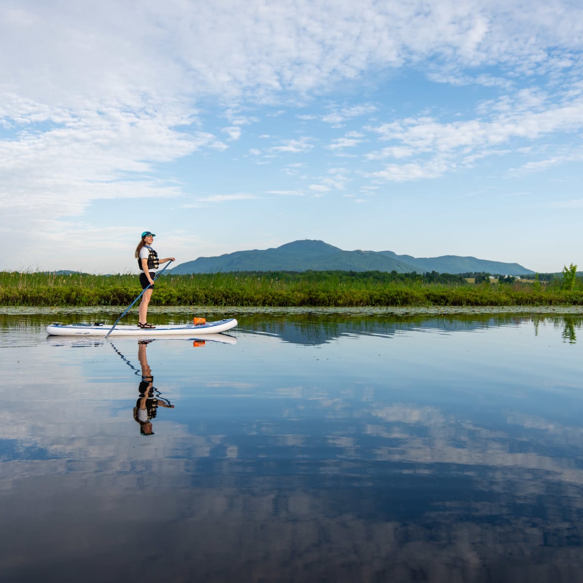 Femme debout sur une planche à pagaie sur la rivière aux Cerises, avec un mont en arrière-plan.