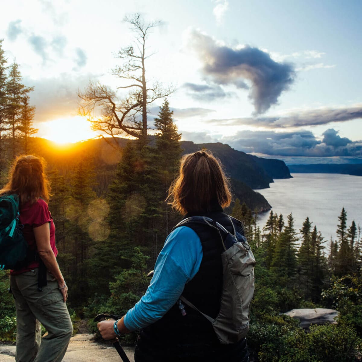 Parc national du Fjord-du-Saguenay - Two women on top of a mountain, forest and sunset in the background.