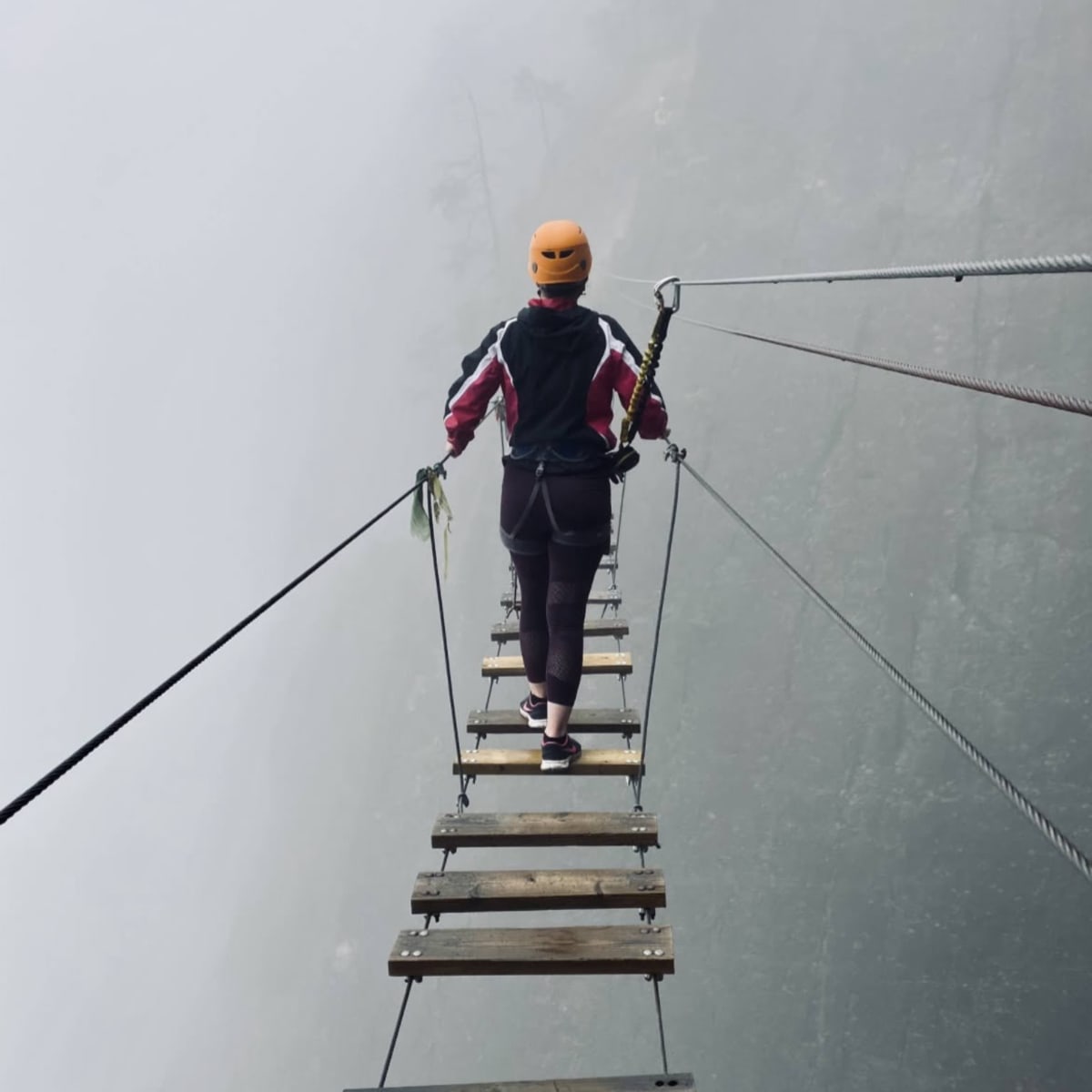 Femme sur un pont suspendue en via ferrata par temps brumeux.