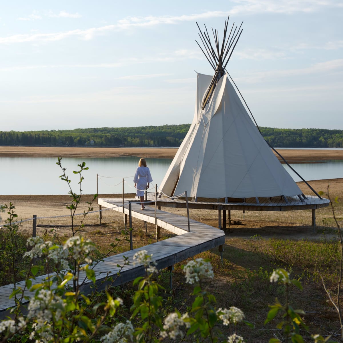 Femme marchant en peignoir marchant à côté d'un tipi sur le bord d'un lac en été.