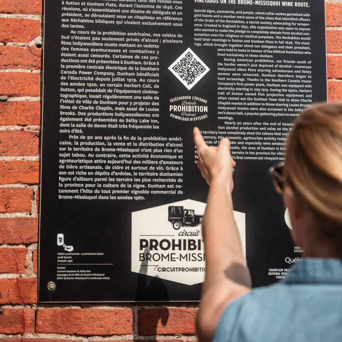 Femme en train de lire une affiche à l'effigie du Circuit de la Prohibition.