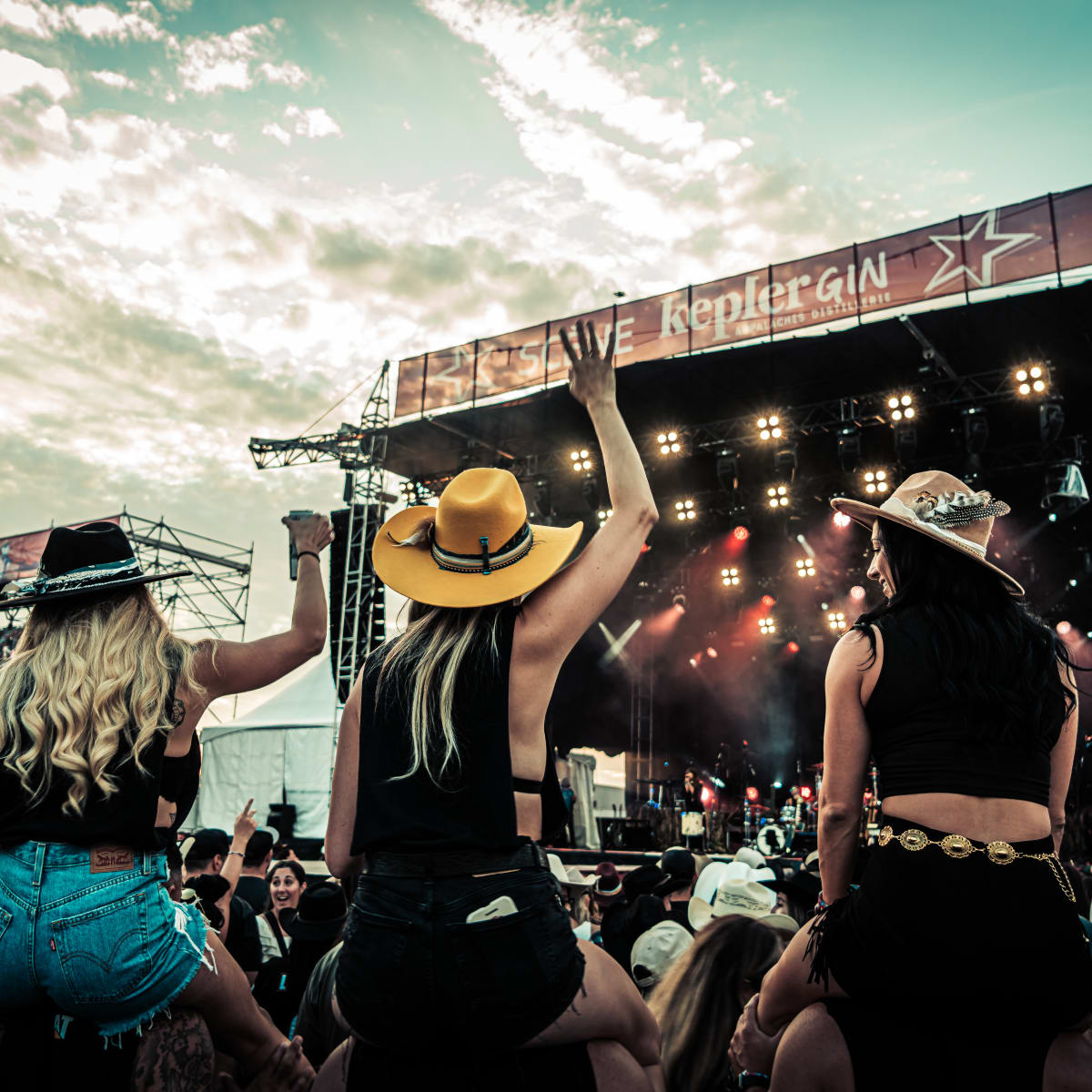Foule à l'extérieure devant une scène avec quatre femmes qui portent des chapeaux de cowboy.