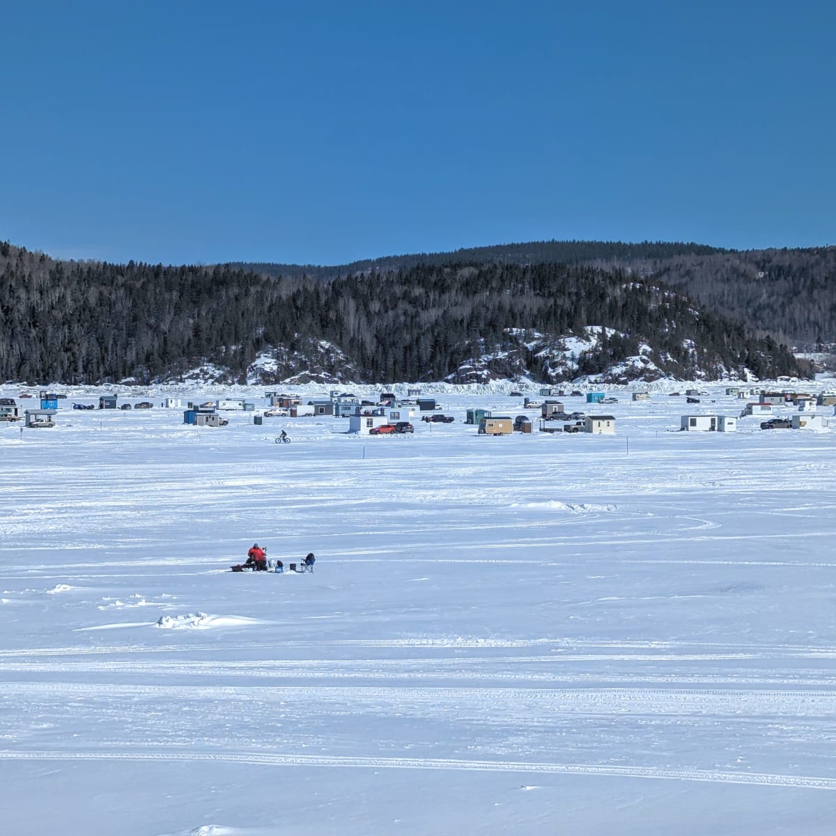 Le fjord du Saguenay enneigé avec des cabanes de pêche qu'on aperçoit au loin.