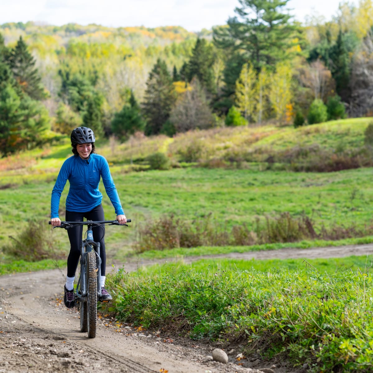 Une femme en vélo sur un sentier en terre dans un décor de début d'automne.