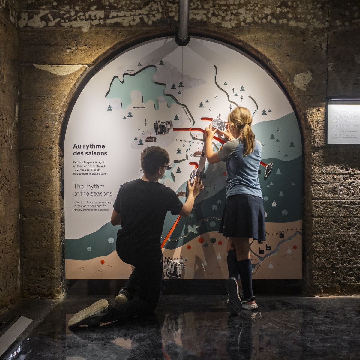 Deux jeunes devant un panneau d'exposition dans une salle en béton.