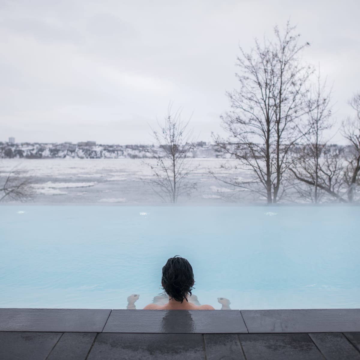Vue de dos d'une personne dans un spa en train de regarder la vue sur le fleuve en hiver.