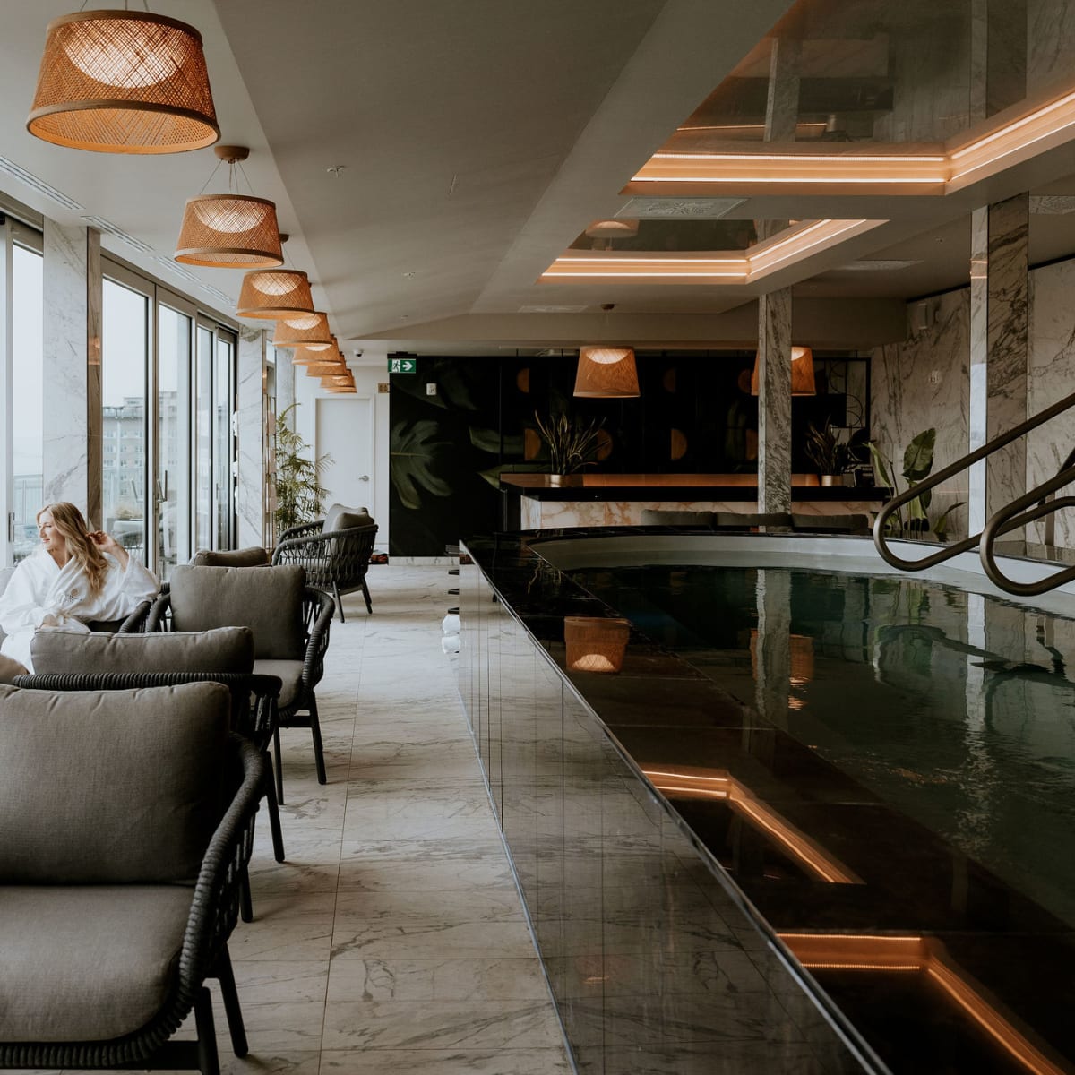 Two people in bathrobes sitting by a Zen-inspired indoor pool, admiring the view outside.