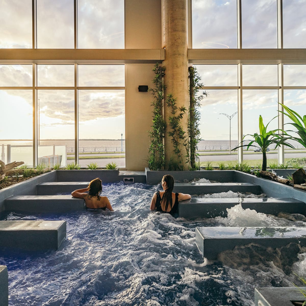 Deux filles dans les bains du Noah Spa qui regardent le fleuve par la baie vitrée.