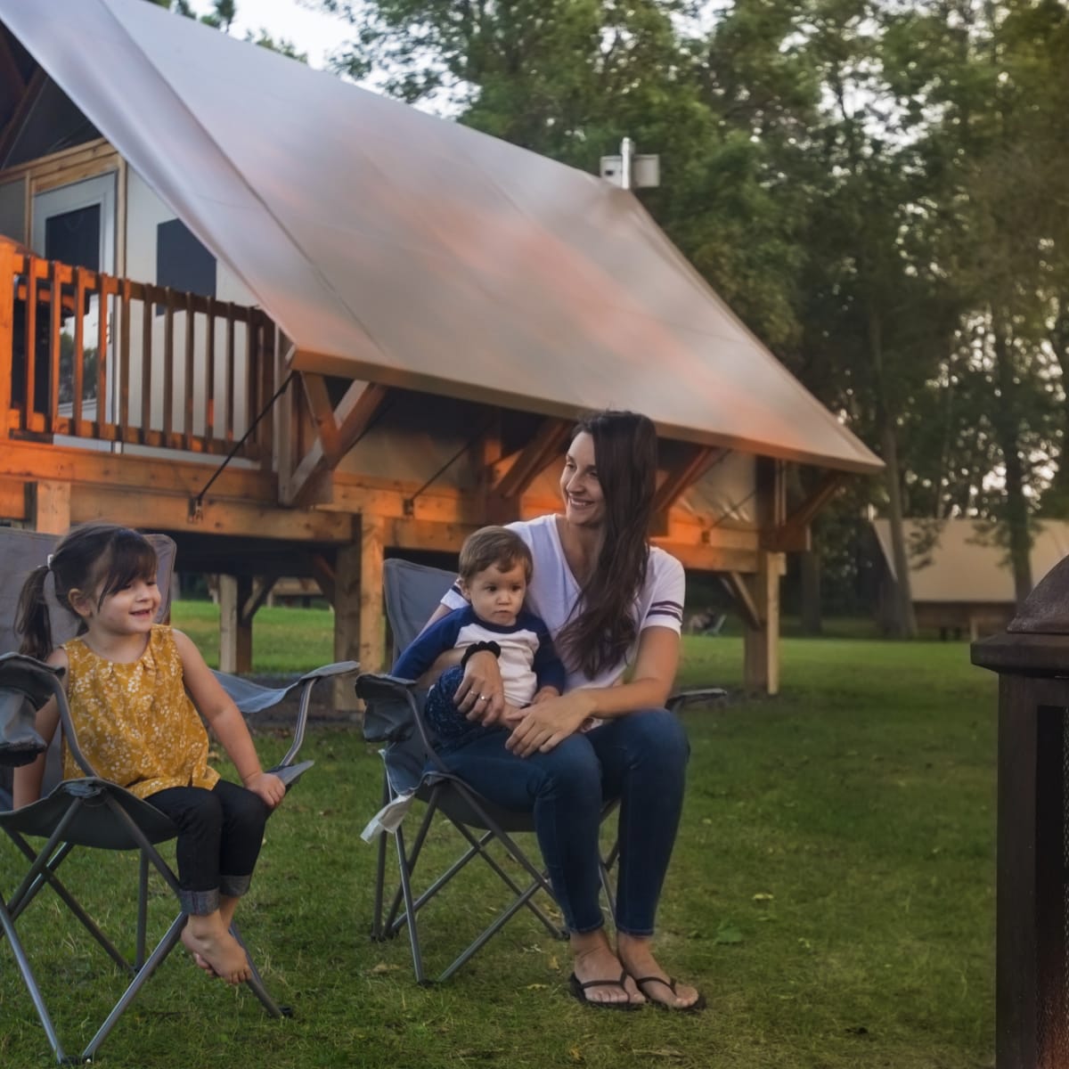 Mère et ses deux enfants au bord du feu de camp devant un prêt-à-camper