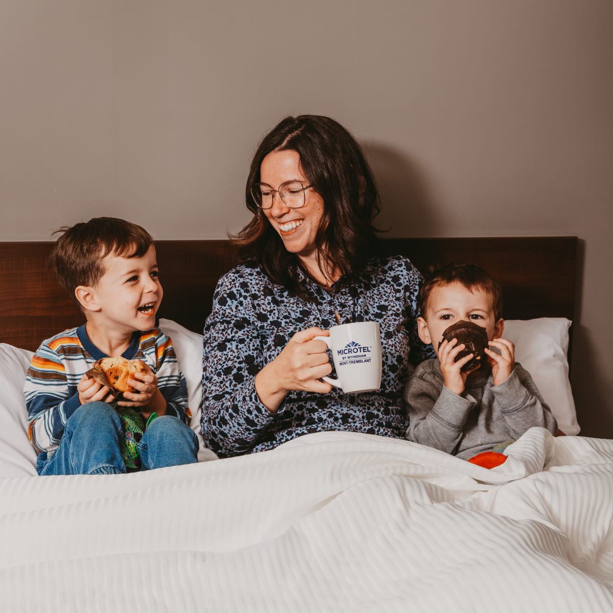Mother and two sons having breakfast in bed at the hotel.