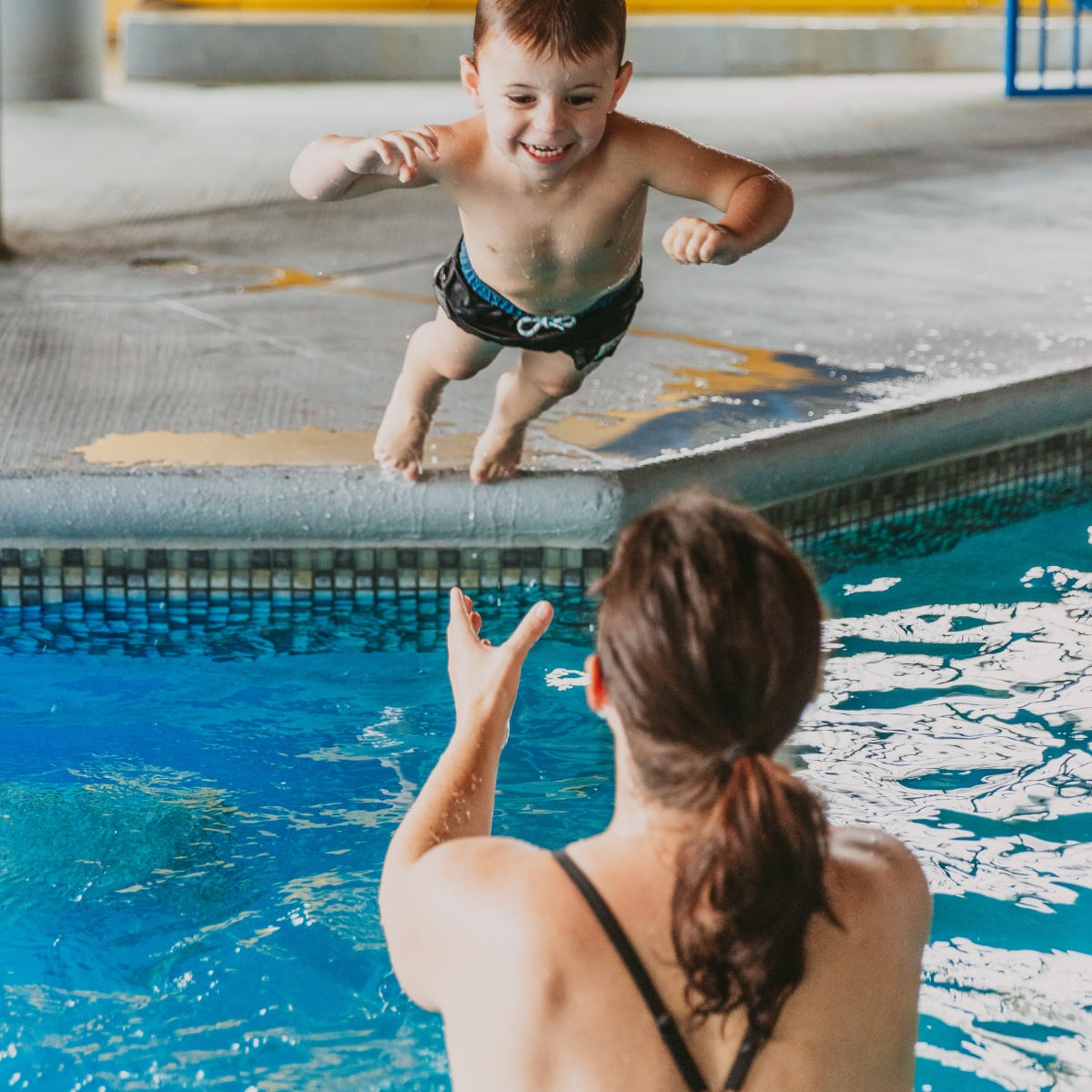Mother in the hotel pool catching her son jumping in the water.