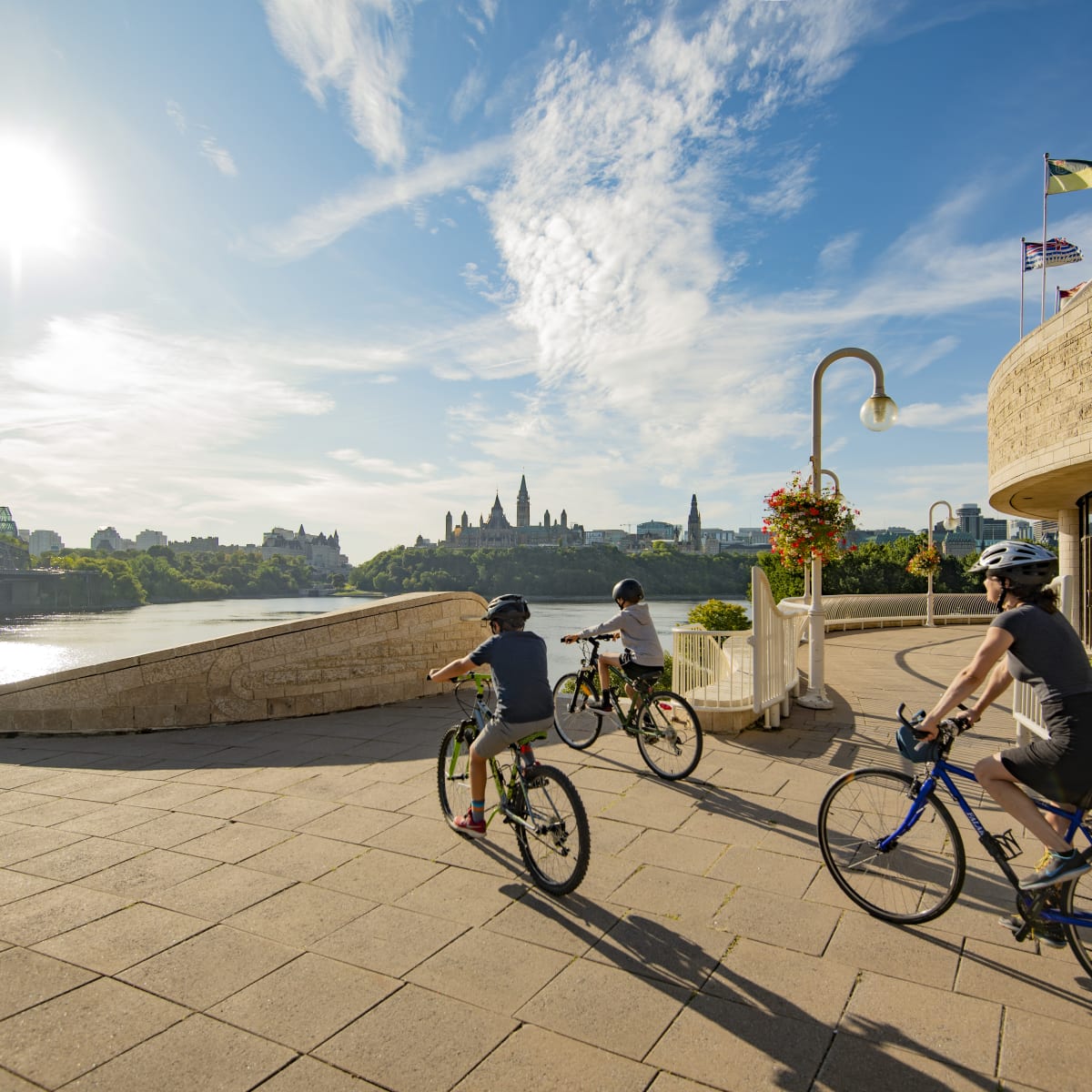 Mother and two sons on bikes next to the Canadian Museum of History in front of the Ottawa River.