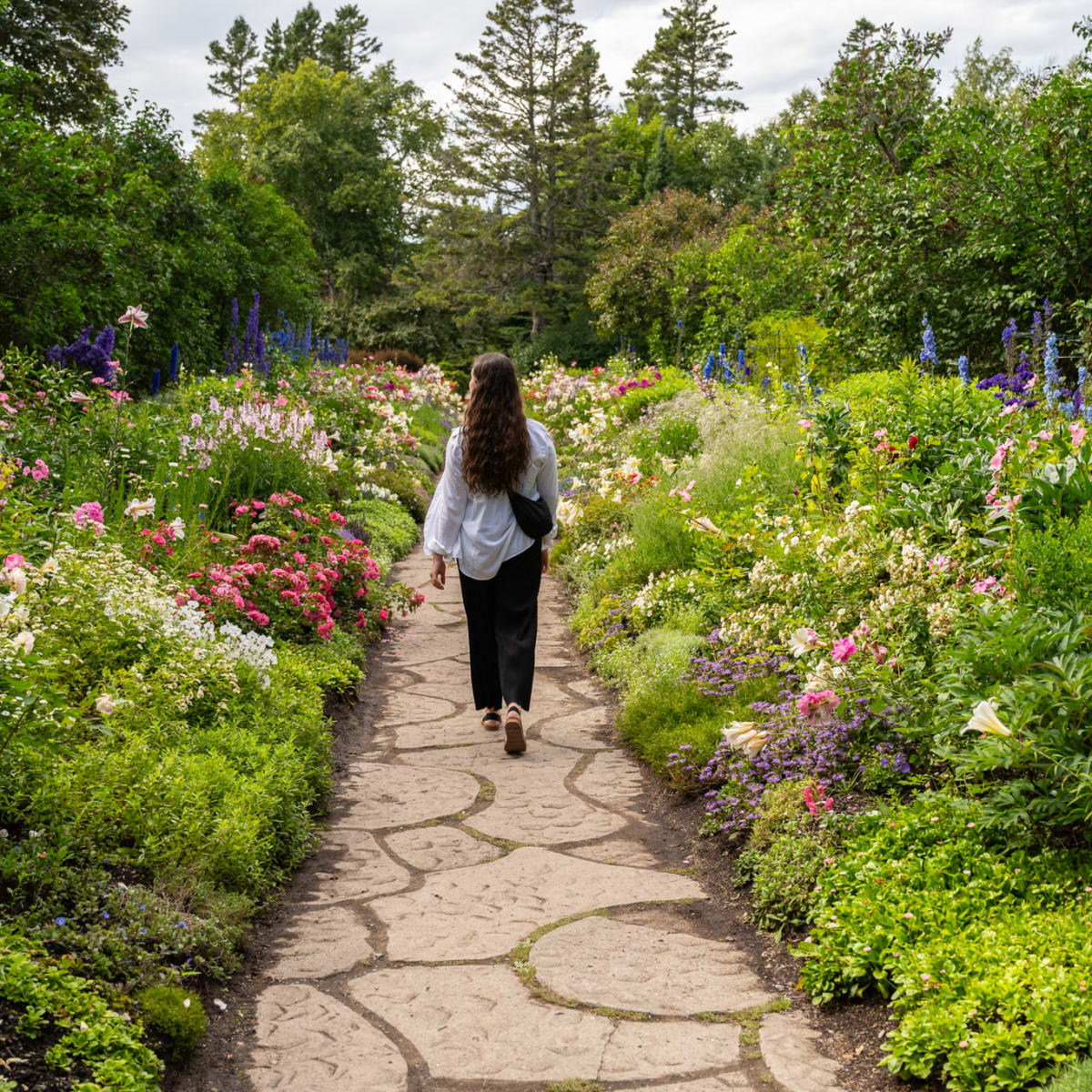 Femme qui marche qui traverse un jardin fleuri.