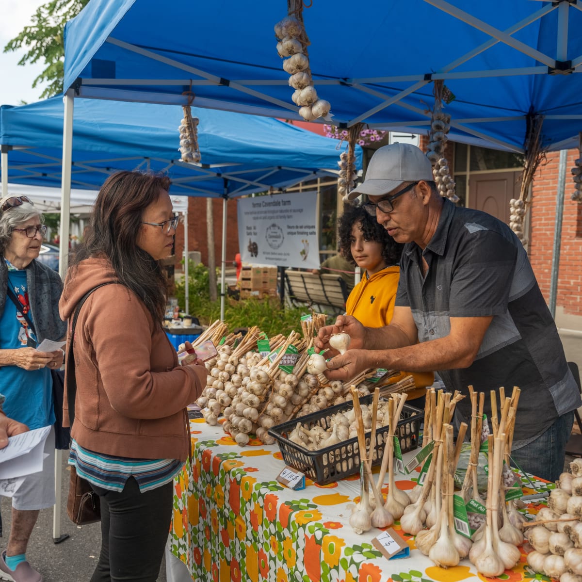 Garlic stand at a market, with vendors and clients discussing.
