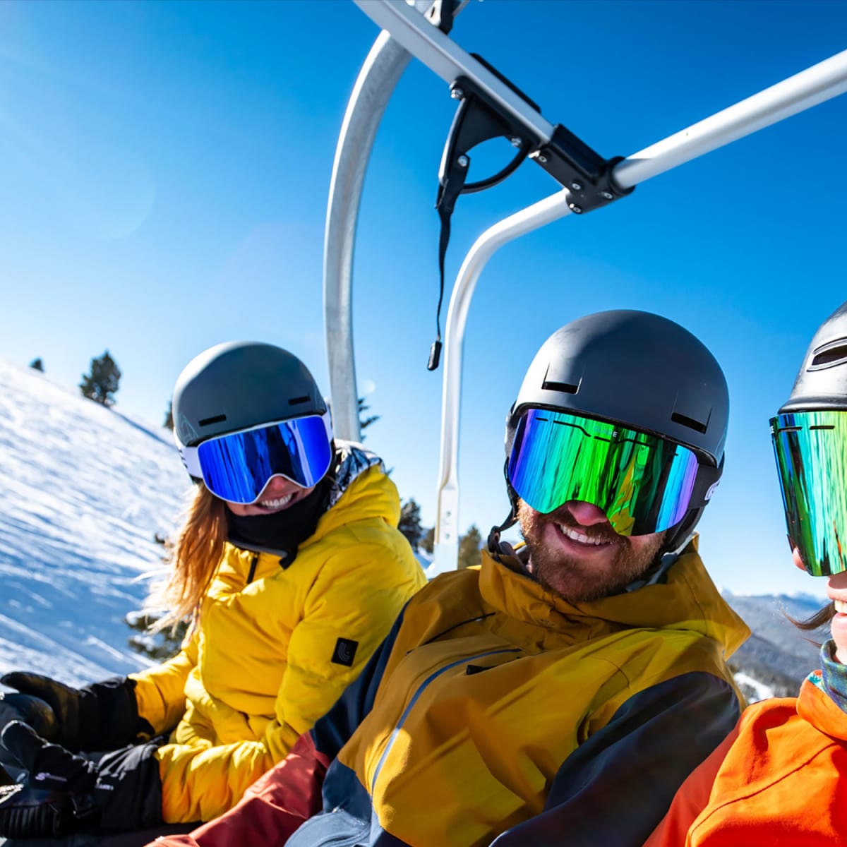 Three skiers in a lift, it's a sunny day and they're smiling.