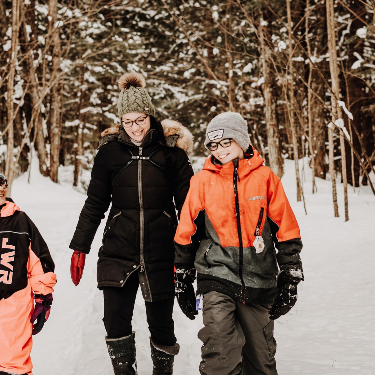 Une mère et deux enfants, tous souriants, dans une forêt enneigée.