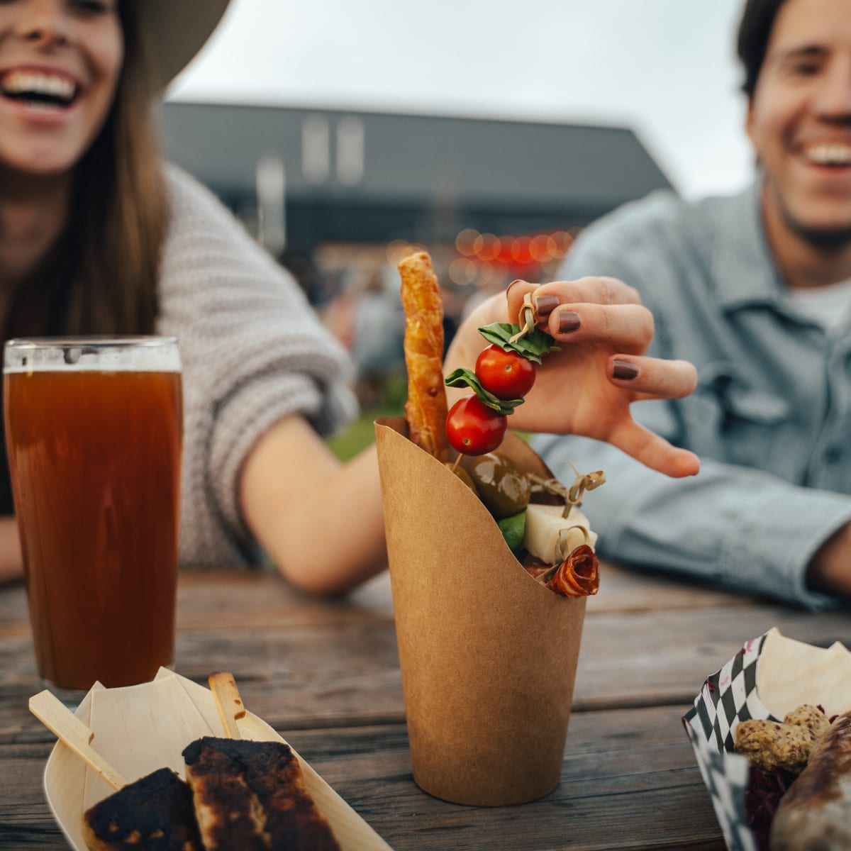 An assortment of food on a table in the foreground, with two happy-looking people sitting at the back.