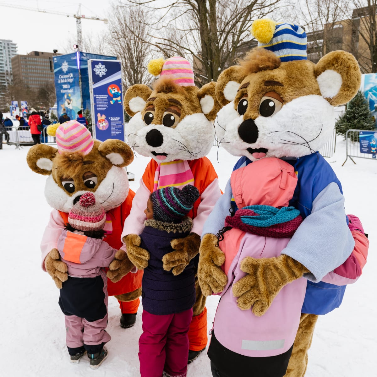 Three mascots outside in the winter giving kids hugs.