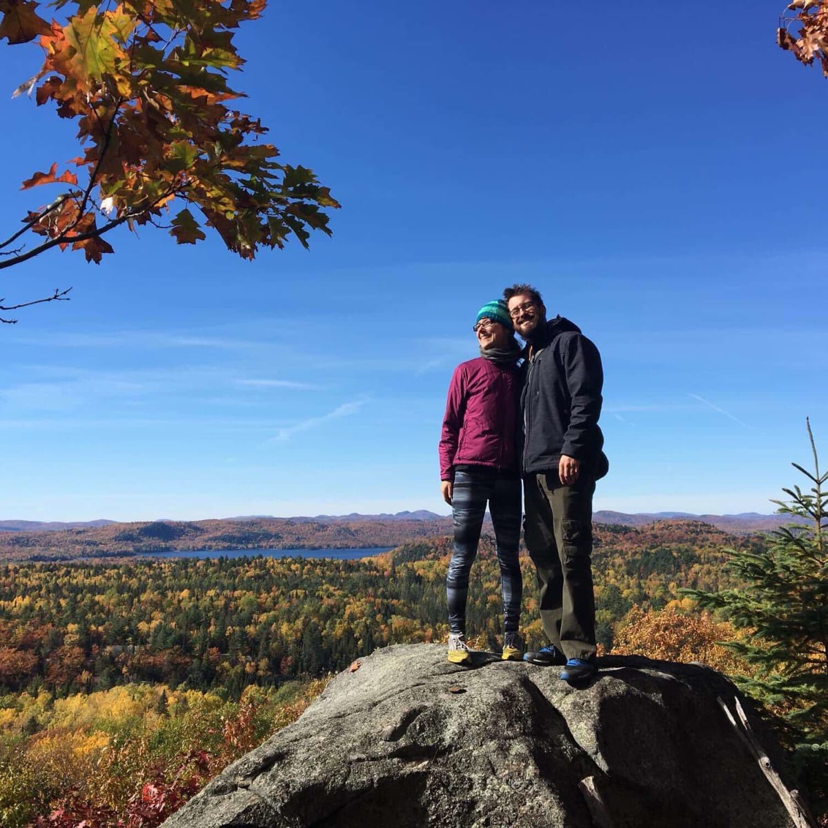 Deux personnes qui prennent la pose sur un rocher devant un paysage d’automne.