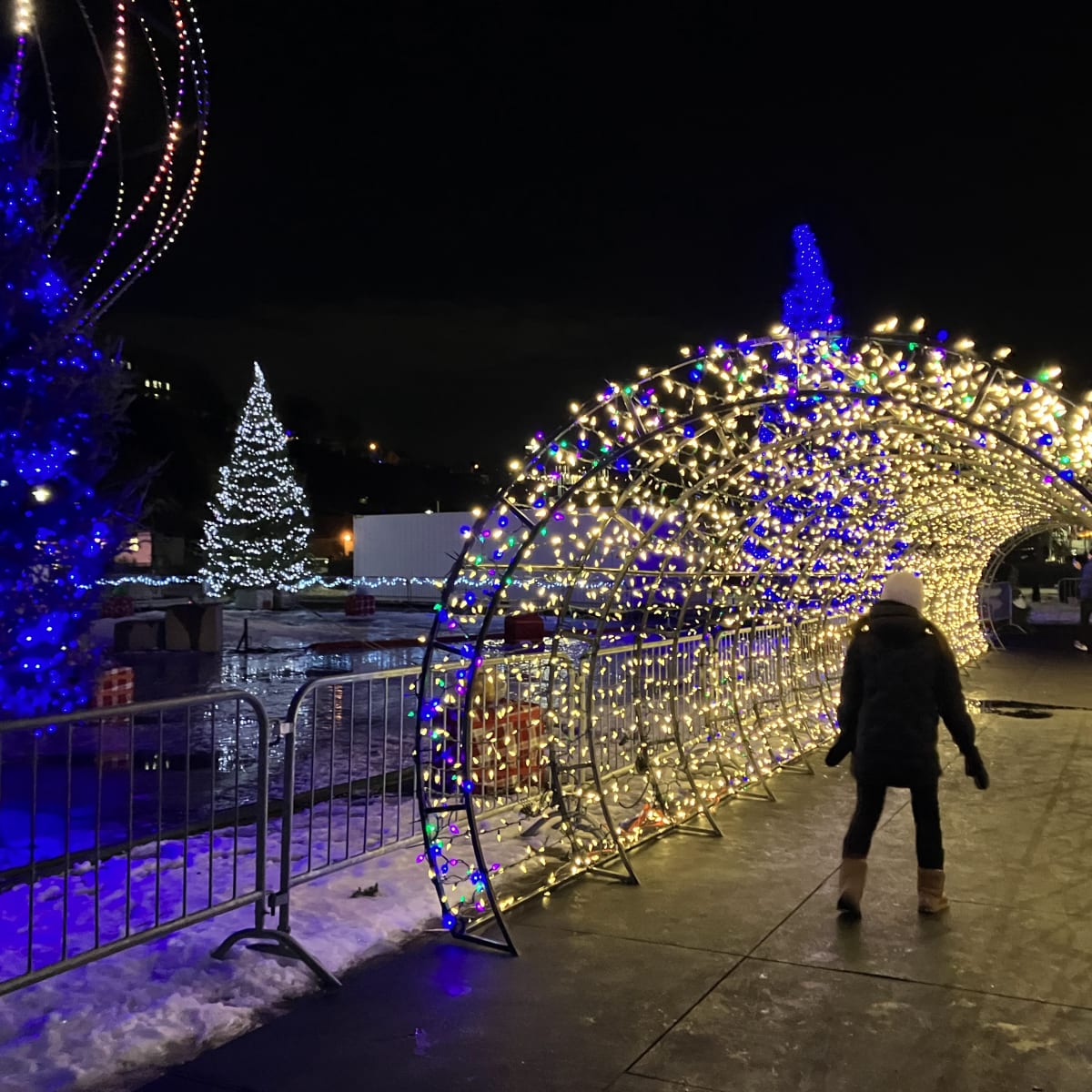 Woman walking under an illuminated arch outside.