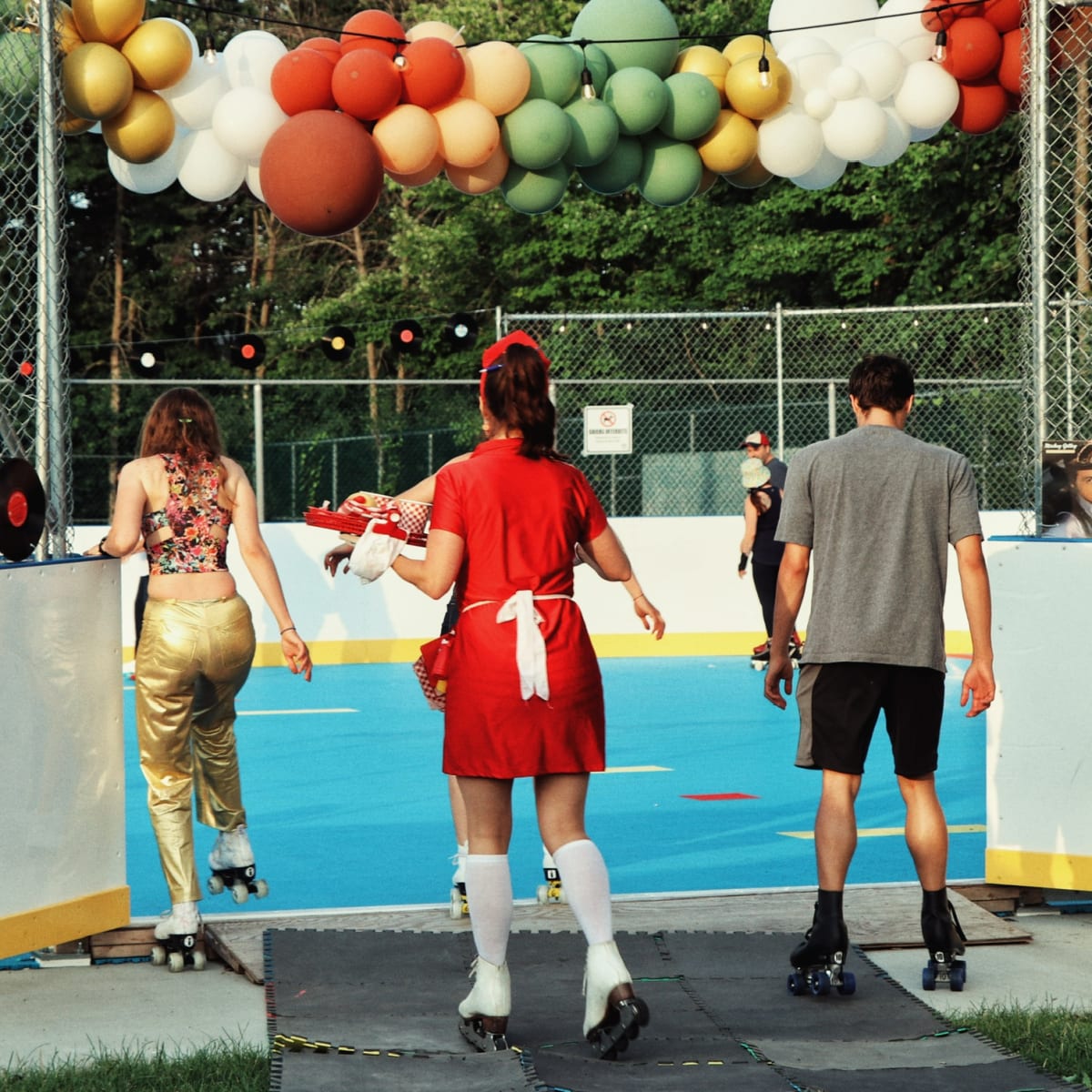 Three people on roller skates preparing to enter a rink decorated with balloons.