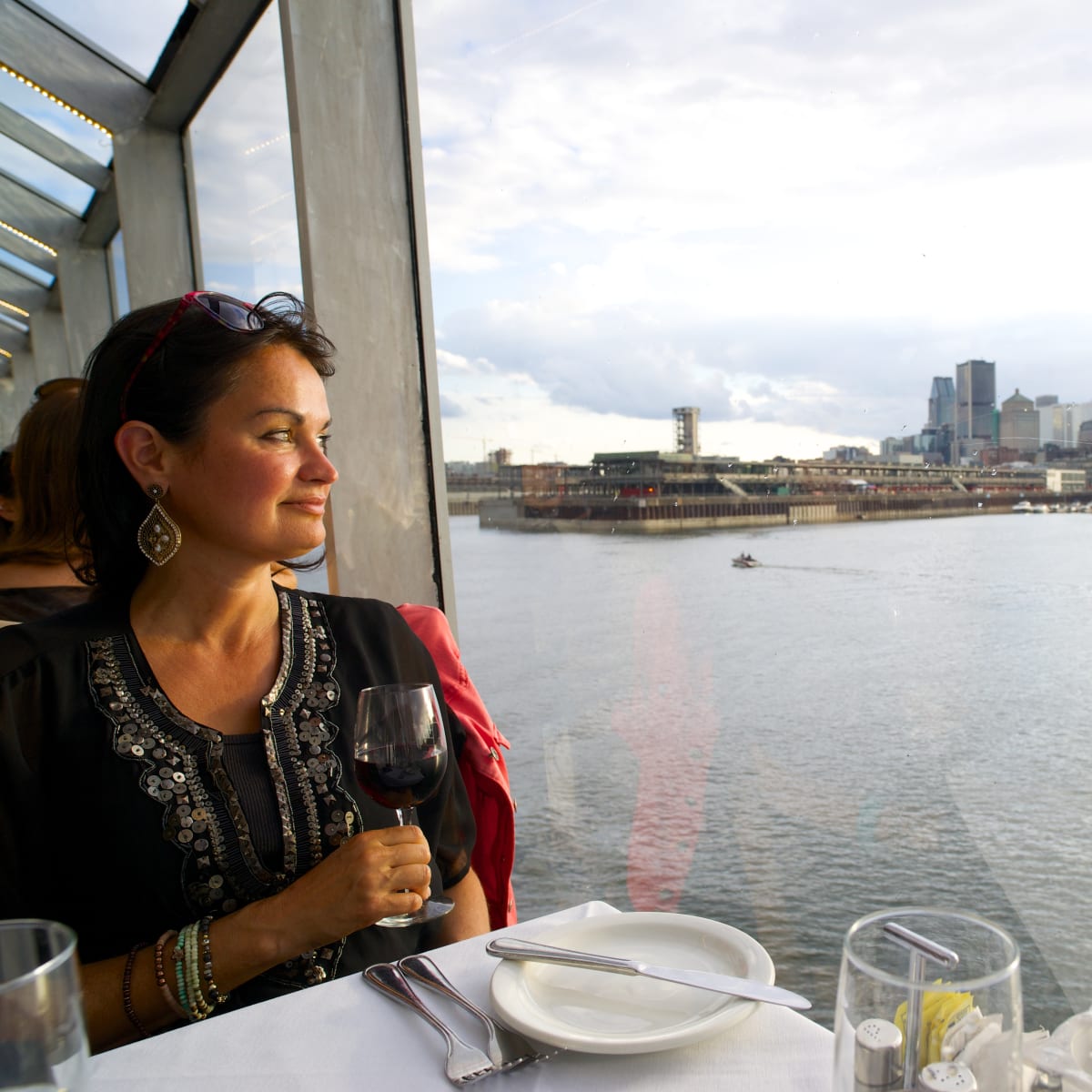 femme avec un verre de vin à bord d'un bateau de croisière qui admire la vue de Montréal.